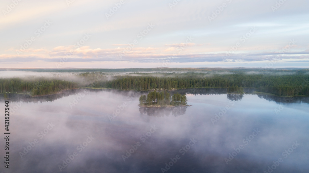 Island with pine trees in morning fog on lake at sunrise. Mysterious island. Atmospheric sunrise over summer forest lake. Island with pine trees in morning fog on lake at sunrise. Mysterious island. Atmospheric sunrise over summer forest lake.