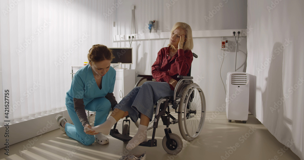 Rehabilitation doctor helping to lift leg of patient in wheelchair