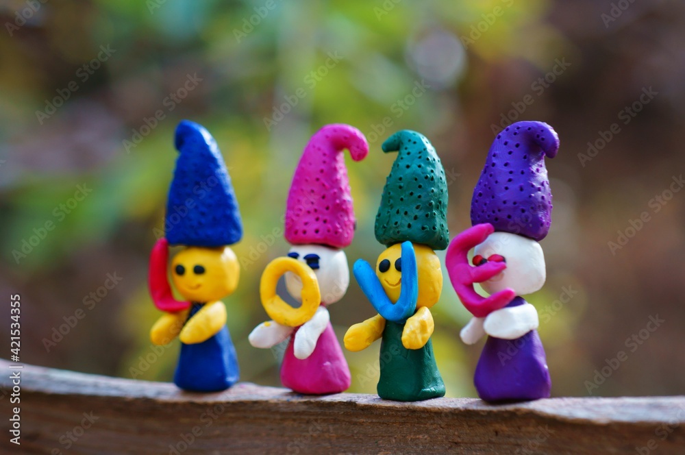 Figures of four fairy-tale dwarfs made of plasticine in the forest on a colored background. The elves have letters in their hands. The inscription love.