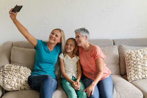 Caucasian mother on couch taking selfie with smiling daughter and grandmother
