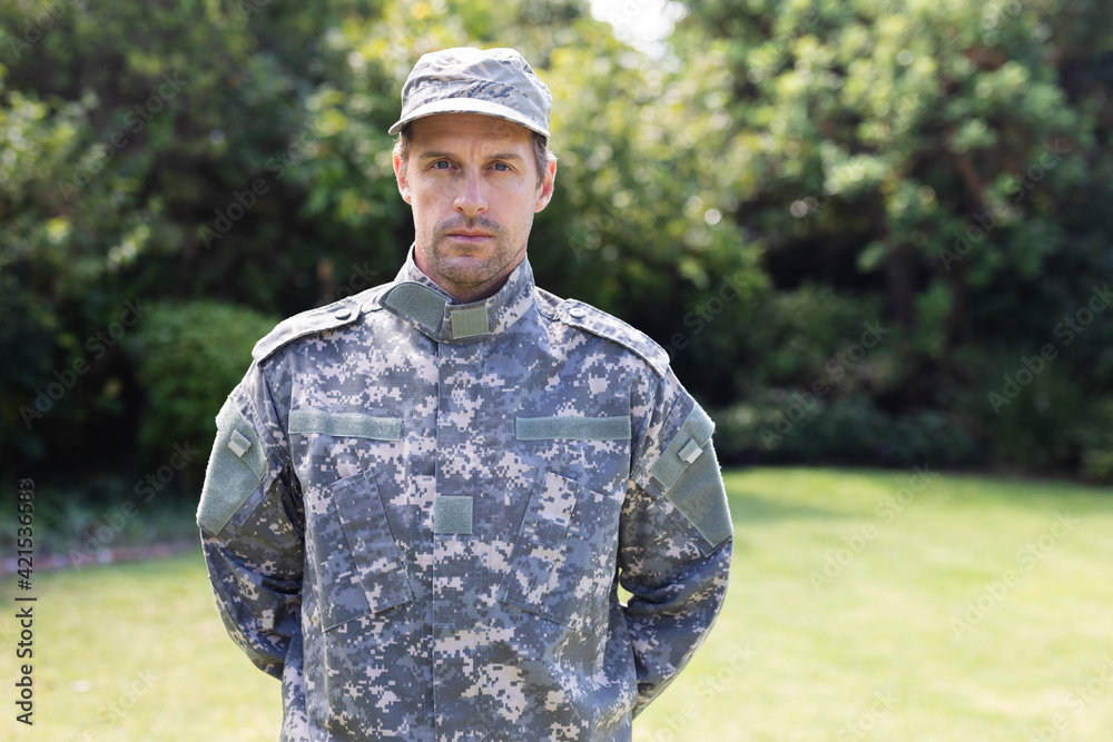 Portrait of caucasian male soldier wearing camo fatigues and cap standing in garden