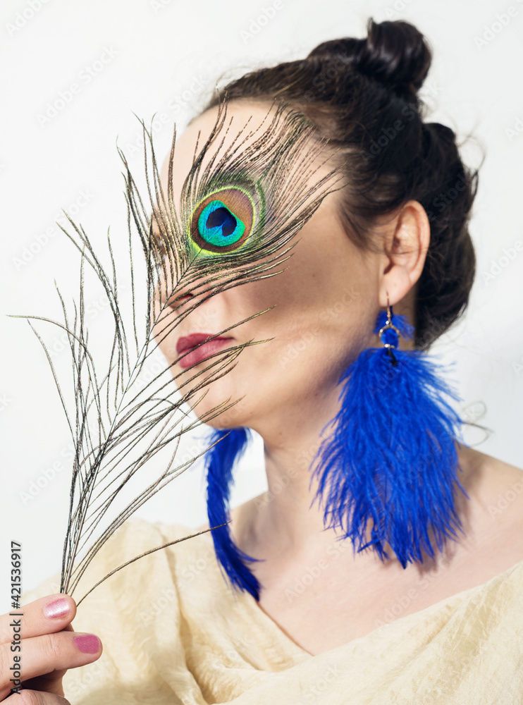 Naklejka premium A woman in blue-feathers earrings and a peackock feather in her hand 