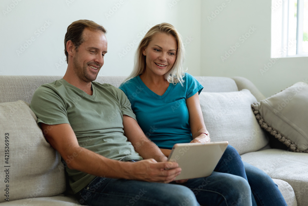 Smiling caucasian couple sitting on couch using digital tablet Smiling caucasian couple sitting on couch using digital tablet