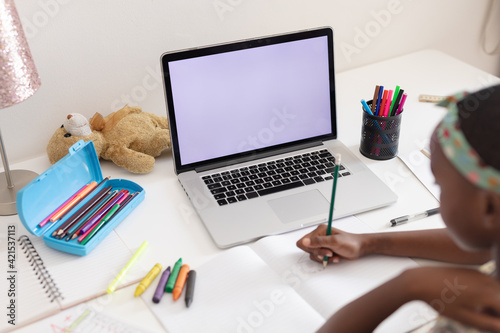 Over shoulder view of african american girl sitting at desk with laptop doing school work