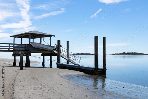 Private boat dock on Tybee Creek at the Atlantic Ocean  sandy beach and still blue waters beneath a bright blue sky with clouds  Tybee Island Georgia  horizontal aspect