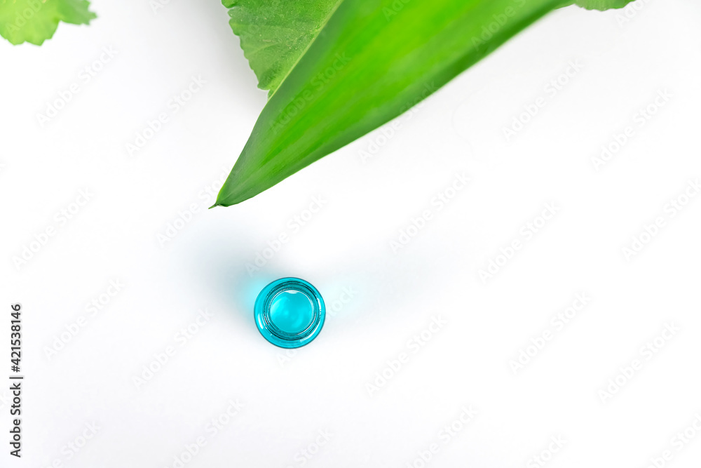 Obraz premium Top view of green plant leaves and a turquoise bottle of serum or oil on a white background with copy space. Flat lay. Concept of cosmetology, medicine