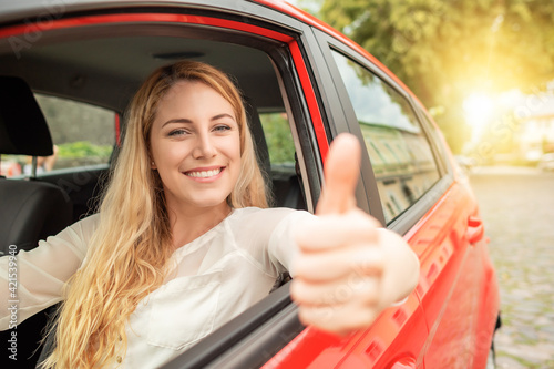 Happy beautiful woman is driving a red car.