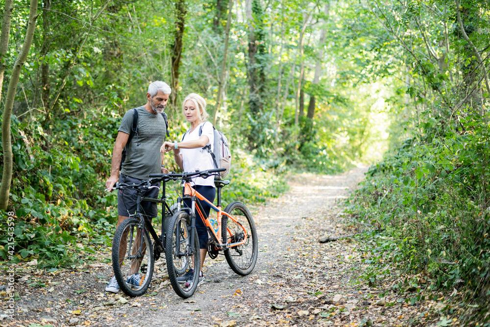 Mature couple checking direction on smart watch in forest Mature couple checking direction on smart watch in forest