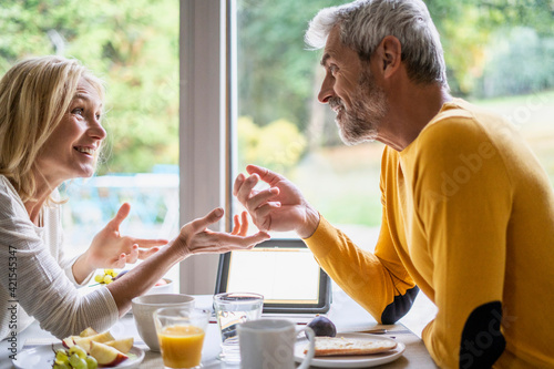 Smiling mature couple talking with each other while having breakfast photo