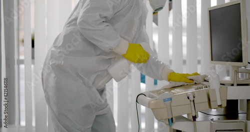 Medical worker in ppe doing sanitization of equipment in hospital room photo