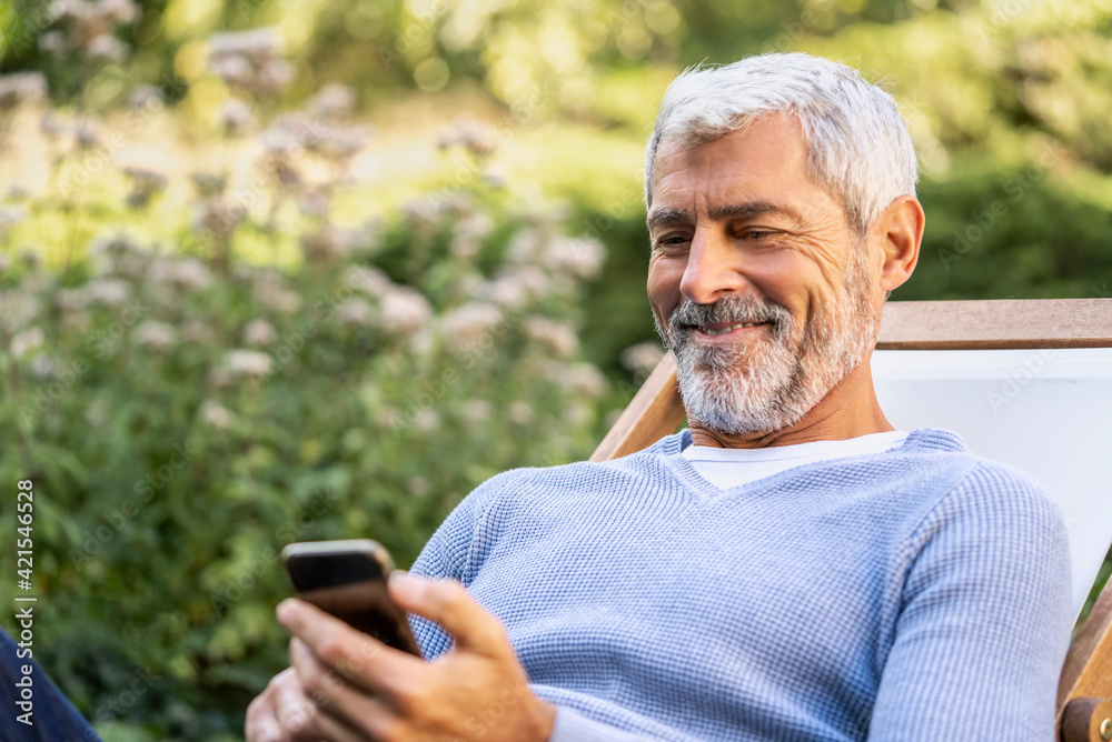 Smiling mature man using smartphone while sitting on deckchair Smiling mature man using smartphone while sitting on deckchair