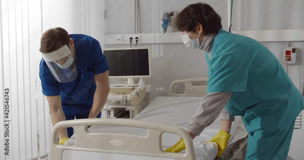 Medical staff changing linen of bed in empty hospital ward Medical staff changing linen of bed in empty hospital ward