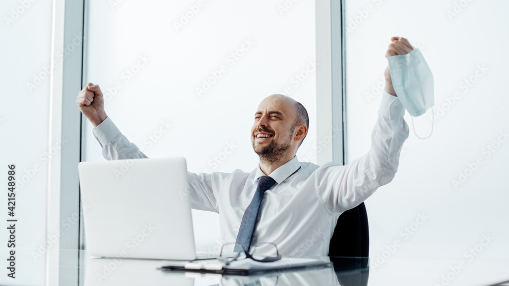 happy businessman with a protective mask in his hand, sitting at his desk.
