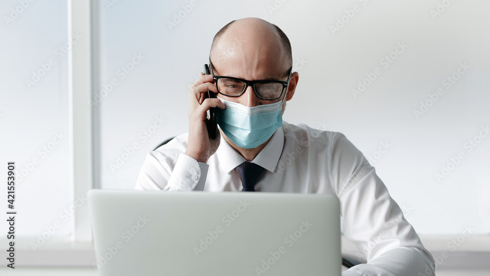 businessman in a protective mask talking on his smartphone at the workplace. businessman in a protective mask talking on his smartphone at the workplace.