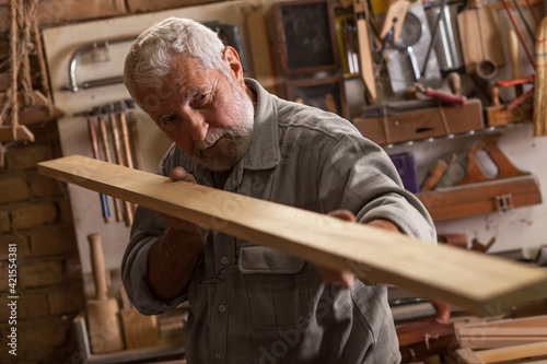 Experienced senior carpenter in his workshop. Measuring the wooden furniture part .