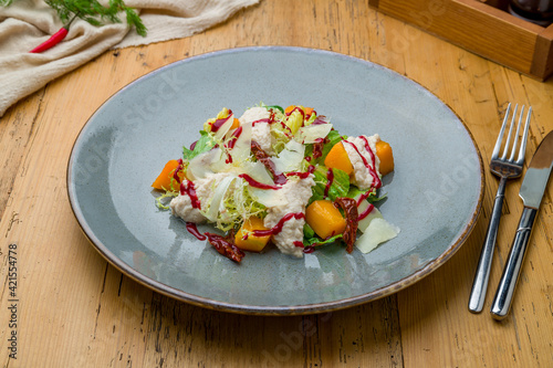 salad with pumpkin, cheese and herbs on grey plate on wooden table