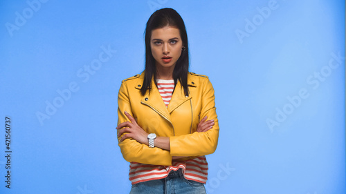 displeased woman in yellow jacket standing with crossed arms isolated on blue