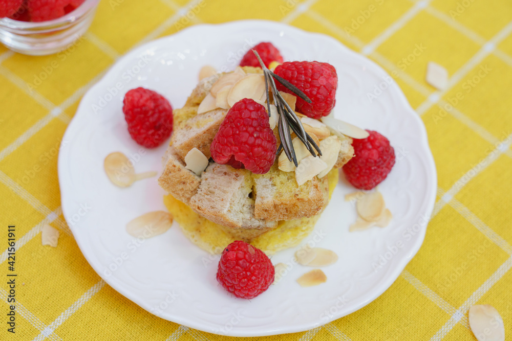 Homemade sweet bread pudding dessert with honey and raspberries in white dish on yellow table blackground. Homemade sweet bread pudding dessert with honey and raspberries in white dish on yellow table blackground.