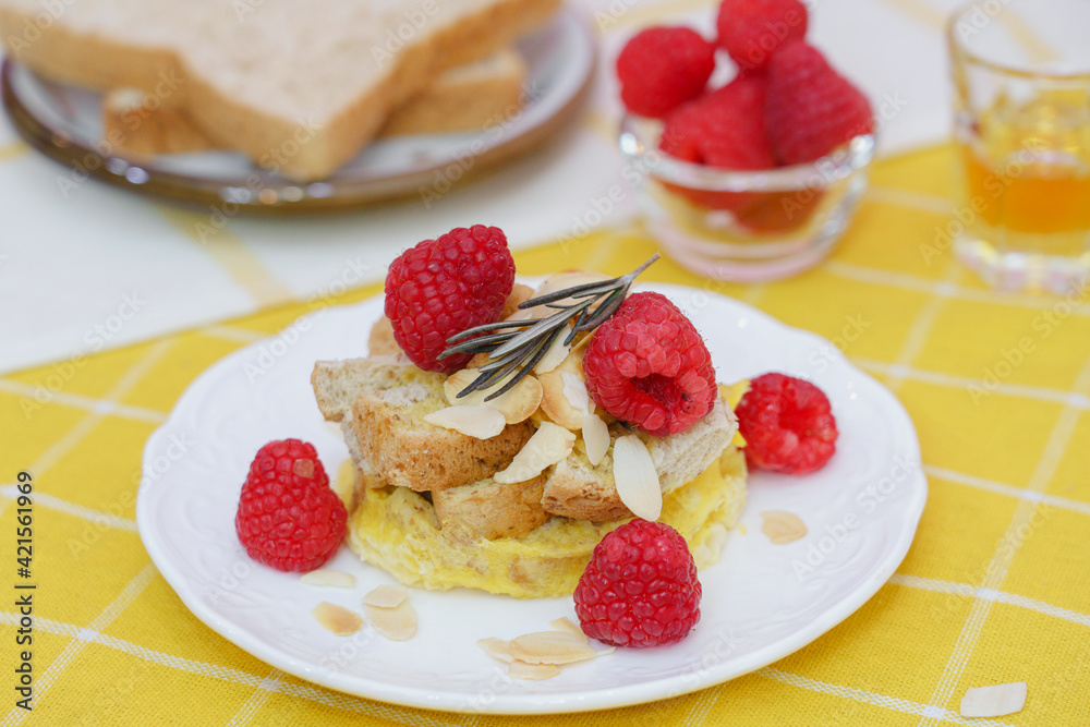 Homemade sweet bread pudding dessert with honey and raspberries in white dish on yellow table blackground.