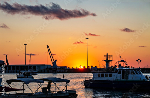 Orange sunset on the black sea in the port with floating yachts and palm trees in the distance against the setting sun, landscape, sunsetscape © Lena_viridis