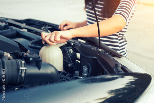 Check auto car's coolant level. That service, repair or maintenance by women hand to open cap of tank or reservoir for filling liquid cooled engine with water, antifreeze in radiator, cooling system. photo
