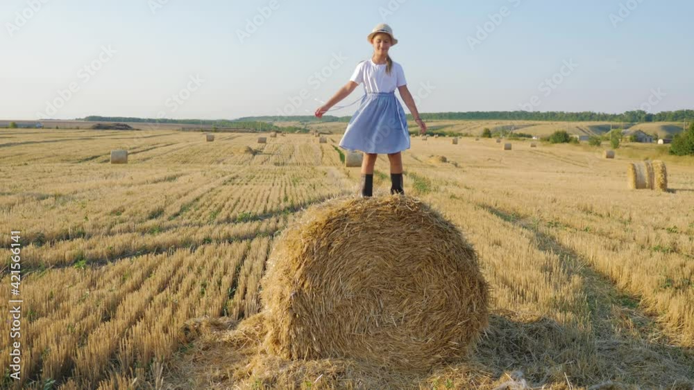 Happy childhood. A happy young girl in a dress and rubber boots is sitting on a haystack in a mown field. Beautiful little girl sitting on a haystack. Fun dream kid concept. Happy childhood. A happy young girl in a dress and rubber boots is sitting on a haystack in a mown field. Beautiful little girl sitting on a haystack. Fun dream kid concept.