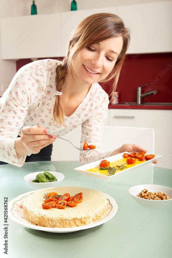 Young blonde caucasian woman smiling and preparing a pesto cheesecake in a kitchen.