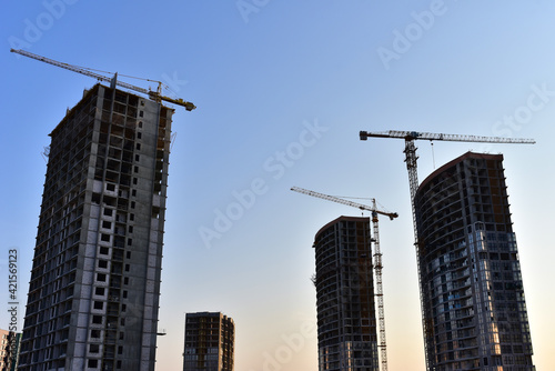 Tower cranes in action at construction site on blue sky background. A crane the conctruct the high-rise building. New residential skyscraper. Tall house renovation project, government programs
