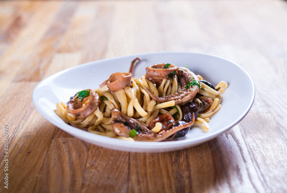 Pasta with calamari seasoned with red cherry olives and basil. Calamari spaghetti on white plate. Mediterranean pasta. seafood. Italian food. Fine dish. Fres food Pasta with calamari seasoned with red cherry olives and basil. Calamari spaghetti on white plate. Mediterranean pasta. seafood. Italian food. Fine dish. Fres food