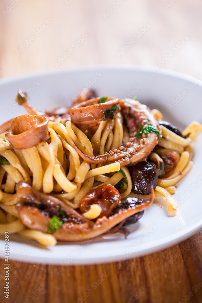 Pasta with calamari seasoned with red cherry olives and basil. Calamari spaghetti on white plate. Mediterranean pasta. seafood. Italian food. Fine dish. Fres food Pasta with calamari seasoned with red cherry olives and basil. Calamari spaghetti on white plate. Mediterranean pasta. seafood. Italian food. Fine dish. Fres food