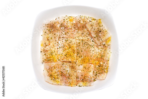 A fresh cod fish fillet cut into squares, sprinkled with spices lying on a white plate, isolated on a white background with a clipping path, top view.