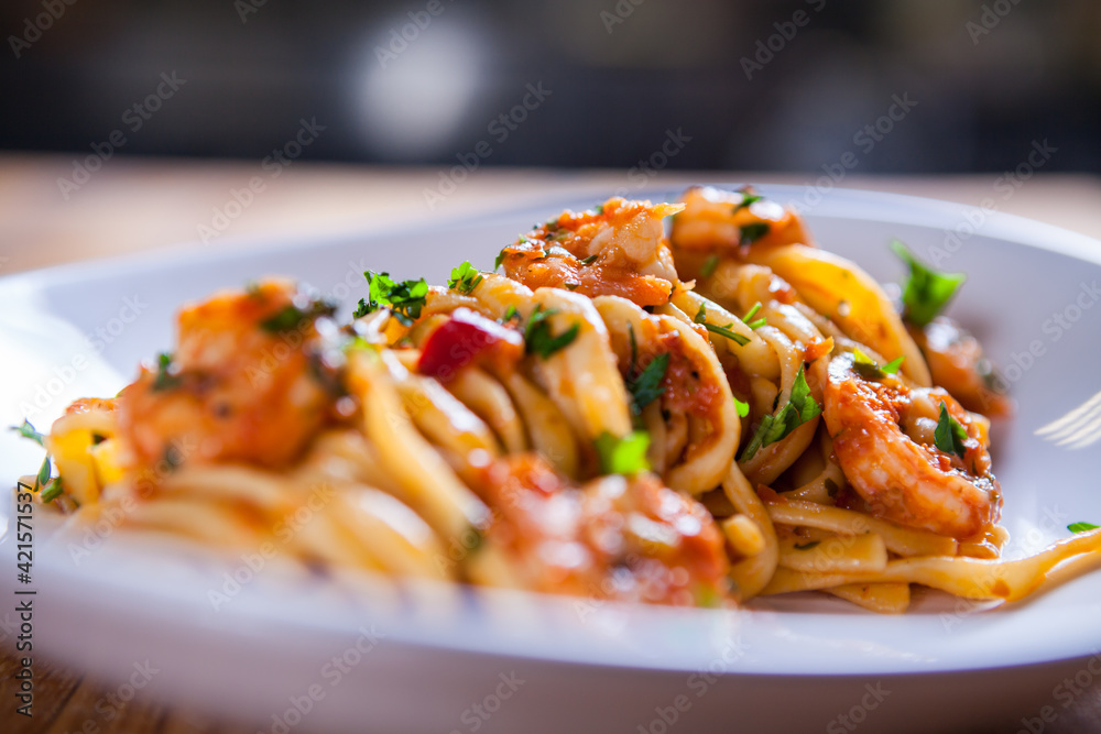 Fototapeta premium Spaghetti with shrimps, parsley and tomato sauce. Shrimps pasta on white plate. Seafood pasta on the wooden table in the kitchen. mediterranean pasta. home made food