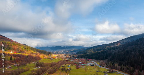 Aerial view of rural village between mountain hills covered with pine forest.