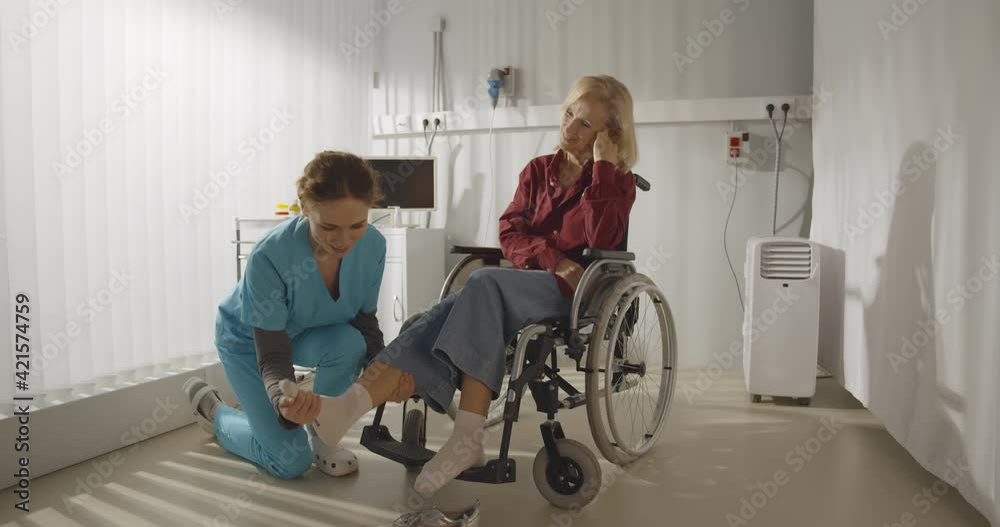 Rehabilitation doctor helping to lift leg of patient in wheelchair Rehabilitation doctor helping to lift leg of patient in wheelchair
