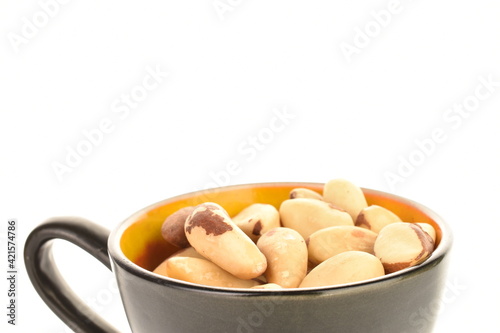 Several ripe organic Brazil nuts in a ceramic cup, close-up. The background is white.