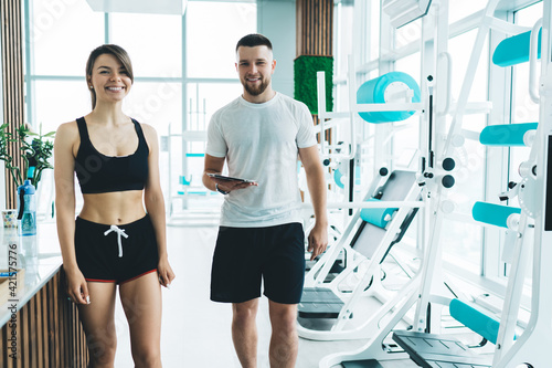 Coach and sportswoman in gym at contemporary machines