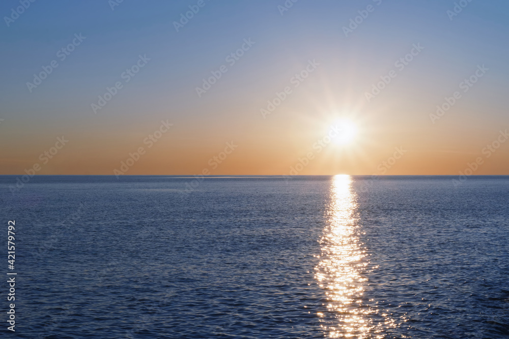 A sunny sunset on the sea stretching into the horizon with a path and highlights on the sea.