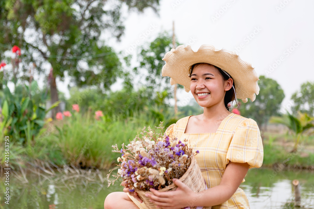 Fototapeta premium Happiness, a beautiful woman in the garden, placed in a hat, holding flowers.