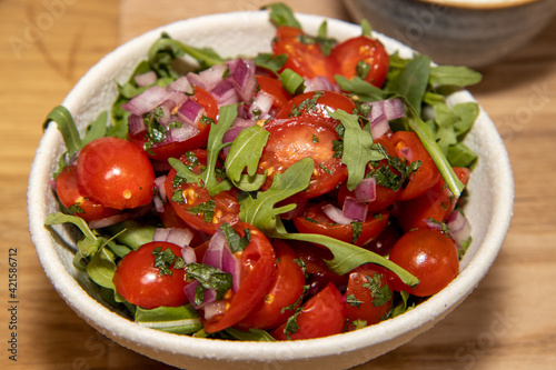A bowl of tomatoes and herbs on a wooden table