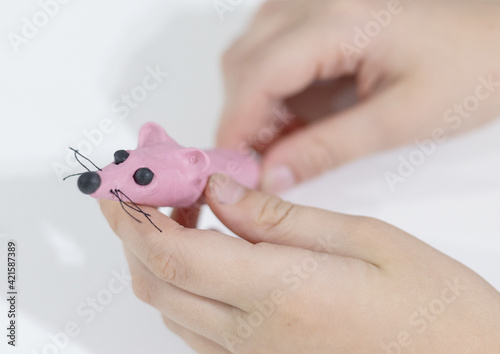 pink mouse sausage in boy's hands made of plasticine on a pink background, children's trend toy