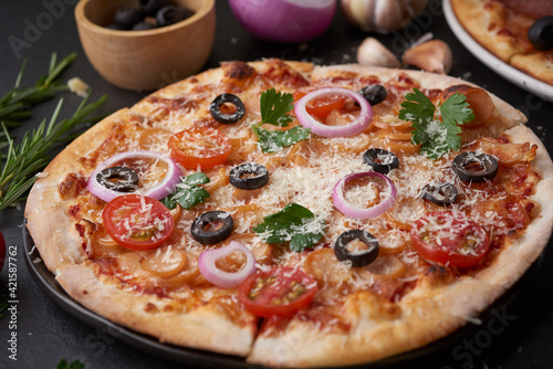 Italian pizza and pizza cooking ingredients on black concrete background. Tomatoes on vine, mozzarella, black olives, herbs and spices. Mixture pizza Italian food. Copy Space. Top view.