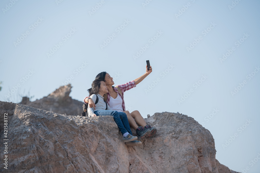 Obraz premium family travel- hikers with backpack looking at mountains, mother with child, Taking selfie,happy mother and girl making self portrait in the mountains, woman holding smartphone camera to take picture.