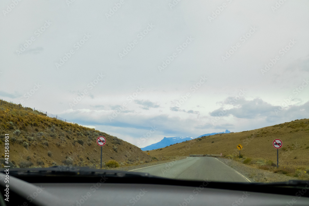 View from a car on a road with road signs with country hills and a mountain in the background with space for text, double lane prohibited signs and a curve sign