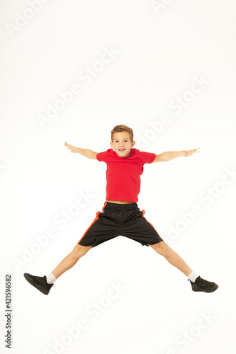 Cheerful male child in sportswear jumping in studio