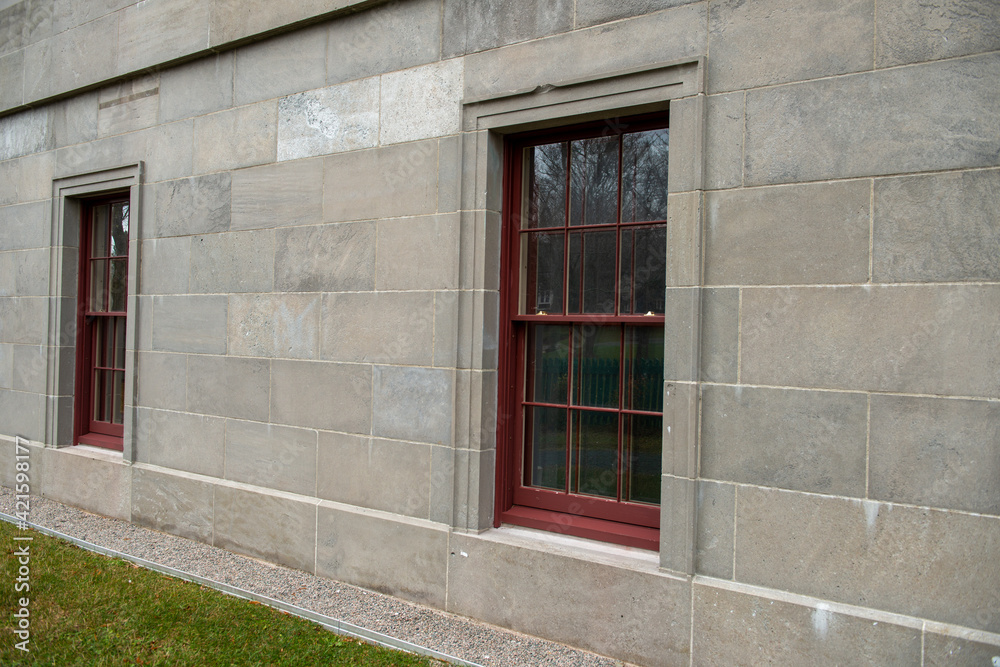 A historic building from the ground floor.The government building has large granite bricks with single double hung wooden windows painted red.