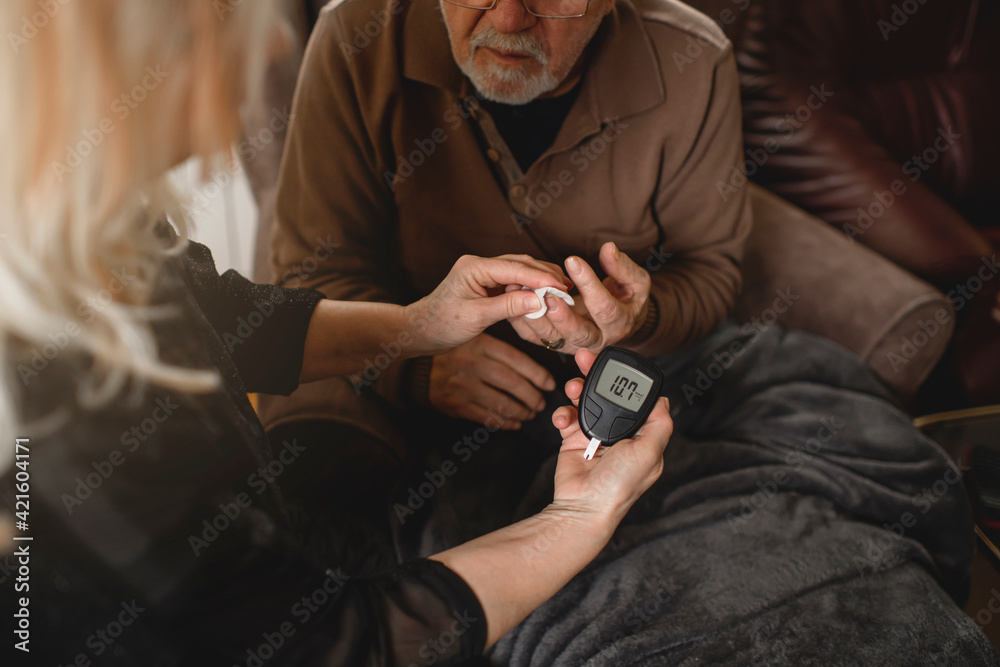 Senior woman checking blood sugar of her diabetic husband at home
