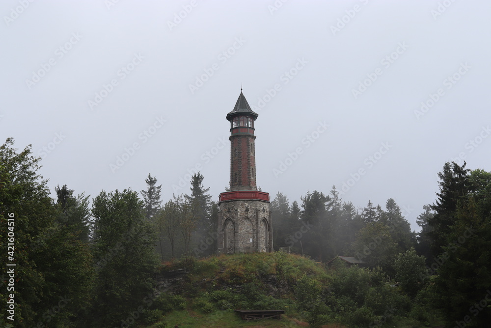 A view to the old stony lookout tower in the forest with leaving fog at Jizera mountains, Czech republic