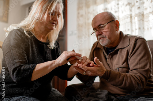 Senior woman checking blood sugar of her diabetic husband at home
