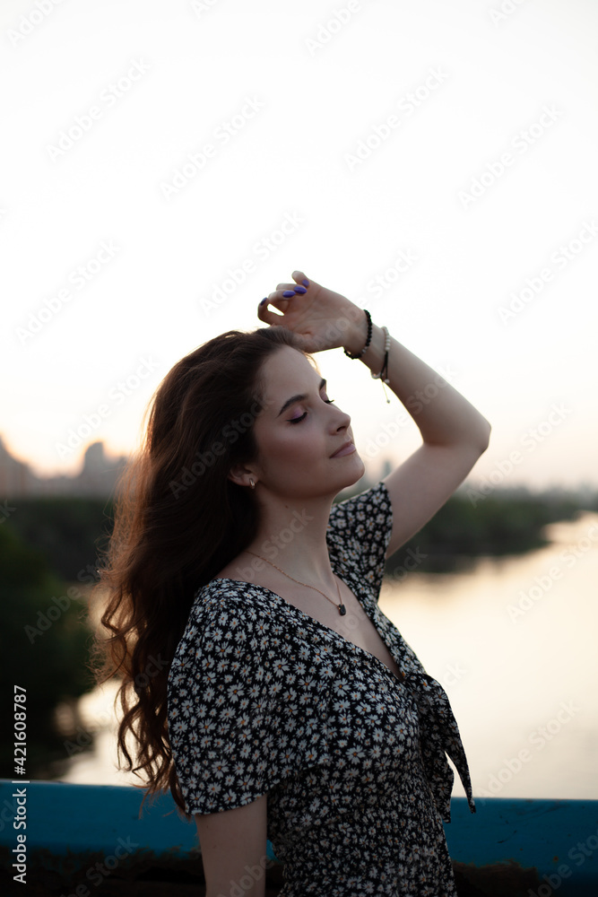 Portrait photo of a young and beautiful woman. Summer time of the year. Happy woman stands on the bridge overlooking the city
