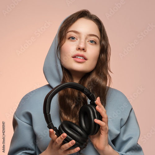 A beautiful young girl is holding overhead studio headphones and looking at the camera.